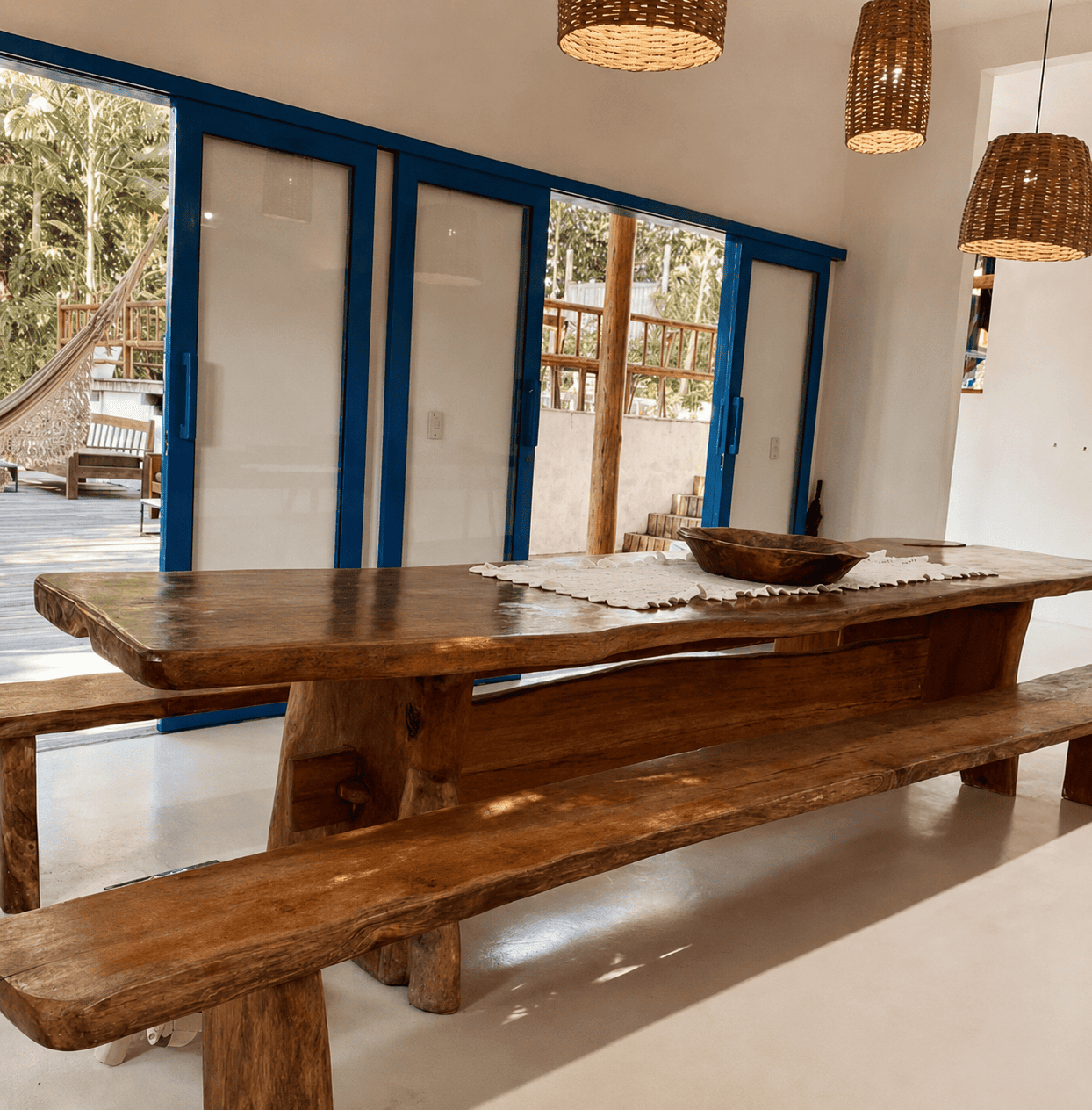 Sala de jantar com mesa de madeira maciça diante das portas azuis.