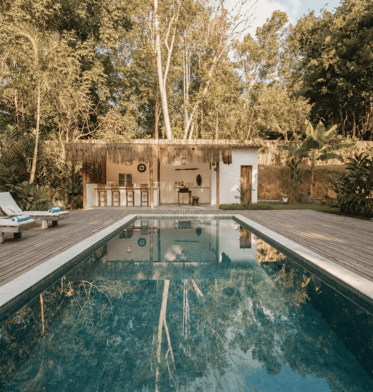 Piscina com deck de madeira cercada por vegetação tropical.